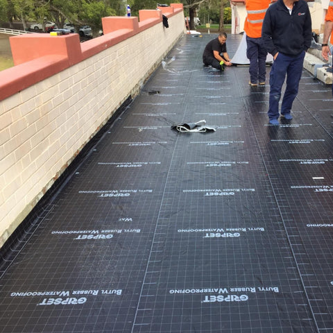 Workers installing Gripset BRW-HD self-adhesive butyl waterproofing membrane on retaining wall for instant leak-proof seal.